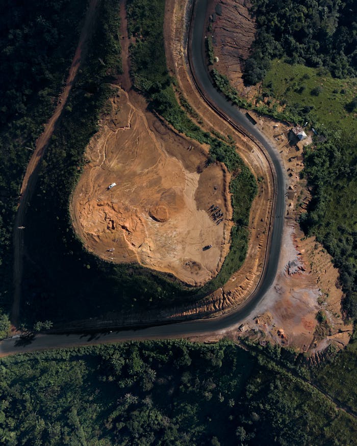 Aerial shot showcasing a winding road next to a quarry amidst lush greenery.