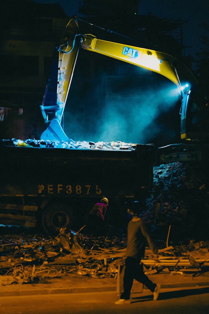A nighttime scene on a construction site with a bulldozer and silhouettes of workers.